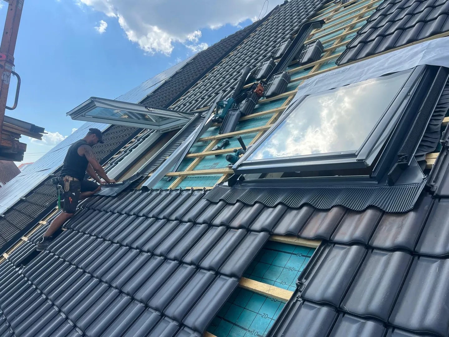 Dachdecker montiert Dachfenster und schwarze Ziegel bei einer Dachsanierung
