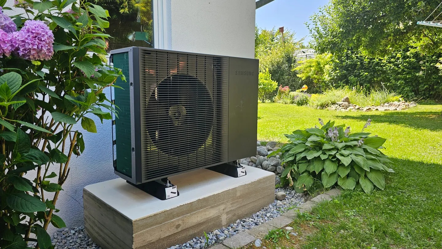 Außeneinheit einer Wärmepumpe neben einem Wohnhaus im Garten
